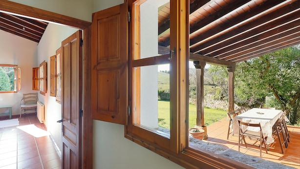 Una habitación con puertas de madera, vista a un jardín y una mesa con sillas afuera.