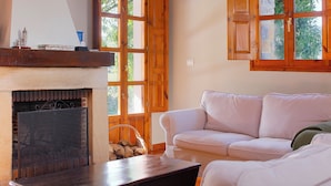 Una habitación acogedora con chimenea, un sofá blanco y ventanas de madera.