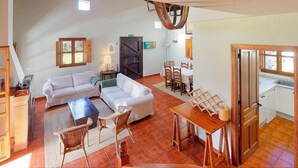 Una sala de estar con un sofá, una mesa de comedor con sillas, una zona de cocina y una escalera.