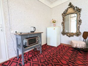Une pièce avec un coin cuisine, un réfrigérateur blanc, un miroir doté d’un cadre orné et une moquette à motifs.
