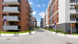 Una calle urbana moderna con edificios residenciales de varios pisos, cielo despejado y sin personas ni vehículos visibles.