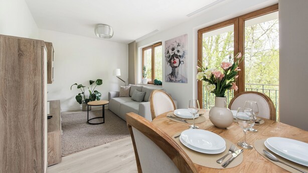 Un comedor con una mesa de madera preparada para dos personas, un sofá y un cuadro en la pared.