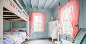 A bedroom with bunk beds, a dresser, a fan, and a chair.