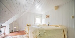 A bedroom with two beds, a wooden chair, a table, and a window.
