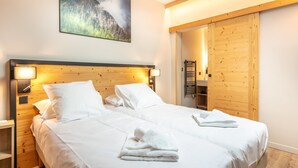 A double bed with white linens, a wooden headboard, bedside lamps, a wooden wardrobe, and a painting of a mountain landscape. - 10-person Apartment With Balcony (Vaujany)