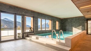 A modern indoor swimming pool with a view of mountains through large windows. - 10-person Apartment With Balcony (Vaujany)