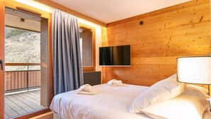 A bedroom with a bed, a TV mounted on the wall, and a balcony with curtains. - 10-person Apartment With Balcony (Vaujany)