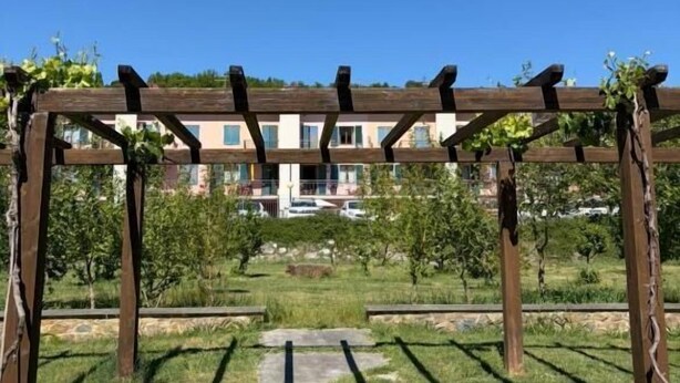 A wooden pergola structure in a garden area with a clear view of a residential building in the background. - Casa di Alice (Barberino Tavarnelle)