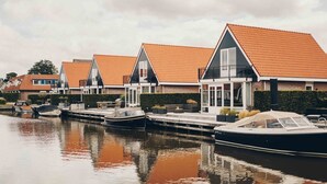 A row of modern houses with red-tiled roofs, a canal, and moored boats. - Parc Pharshoeke - Havenvilla | 6p (Heeg)