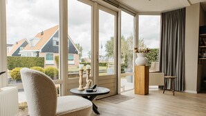 A spacious room with large windows, a round table, a chair, a bookshelf, and a radiator. - Parc Pharshoeke - Havenvilla | 6p (Heeg)