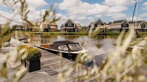 A canal view with a boat docked on a wooden pier, surrounded by houses with gabled roofs. - Parc Pharshoeke - Havenvilla | 6p (Heeg)