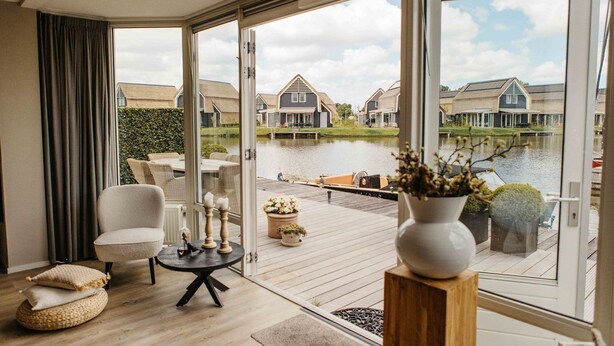 A room with a view of a canal, a wooden deck, and a dining area with outdoor furniture. - Parc Pharshoeke - Havenvilla | 6p (Heeg)
