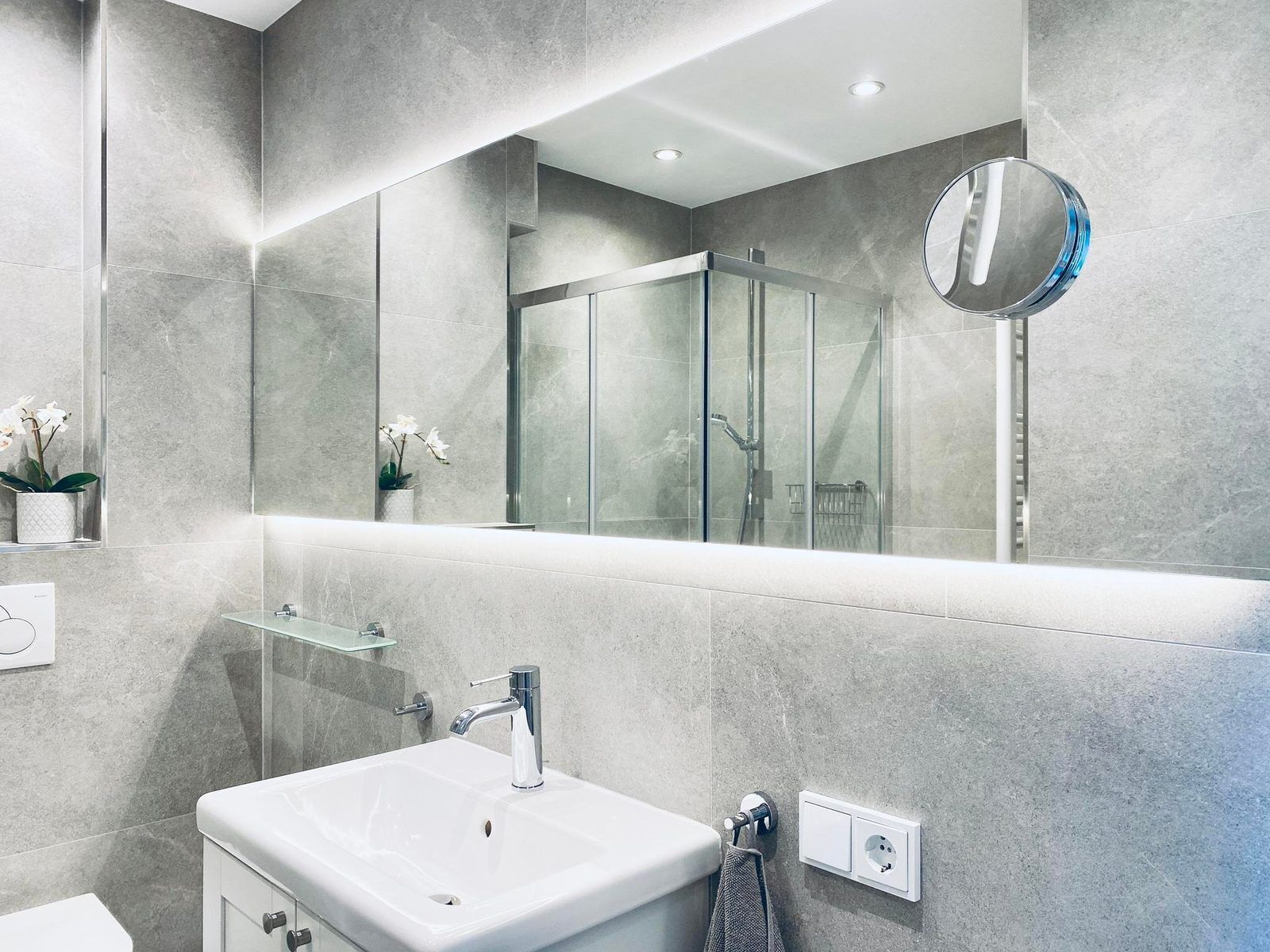 Un ba ño moderno con un espejo grande, cabina de ducha de vidrio y lavamanos blanco.