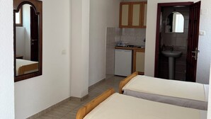 A room with two wooden beds, a small kitchenette, a bathroom with a mirror, and a ceiling light fixture. - Beautiful 1-bedroom apartment with AC in welcoming Budva (Budva)