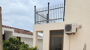 A courtyard with a tiled floor, a metal gate, a potted plant, and a building with a tiled roof and a door. - Beautiful 1-bedroom apartment with AC in welcoming Budva (Budva)