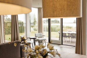 A modern interior with a sofa, chairs, and a table near large windows overlooking a grassy area.