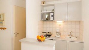 A compact kitchen with a microwave, coffee maker, sink, and a bowl of fruit on the counter.