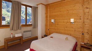 Une chambre avec un grand lit, des murs en bois, une fenêtre avec des rideaux, une table de chevet et un radiateur.