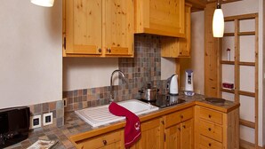 Une cuisine avec des meubles de rangement en bois, un pare-feu en carrelage, un évier, une cuisinière et une bouilloire.