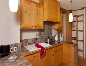 A kitchen with wooden cabinets, a tiled backsplash, a sink, a stove, and a kettle. - Central Alpine Apartment Near Tourist Office (Les Deux Alpes)