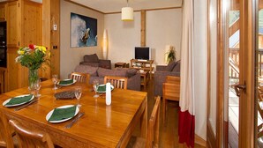 Un coin repas avec une table en bois dressée pour quatre personnes, un canapé, un téléviseur et un tableau accroché au mur.