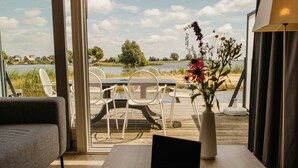 A room with a laptop on a table, a sofa, and a view of a lake with chairs outside. - Parc Pharshoeke - Herenhuis geschakeld | 6p (Heeg)
