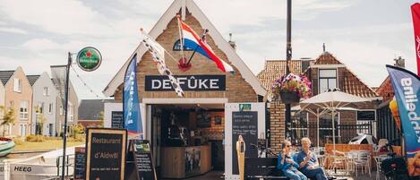 A restaurant named 'DEFÜKE' with a signboard, outdoor seating, and a street lamp.