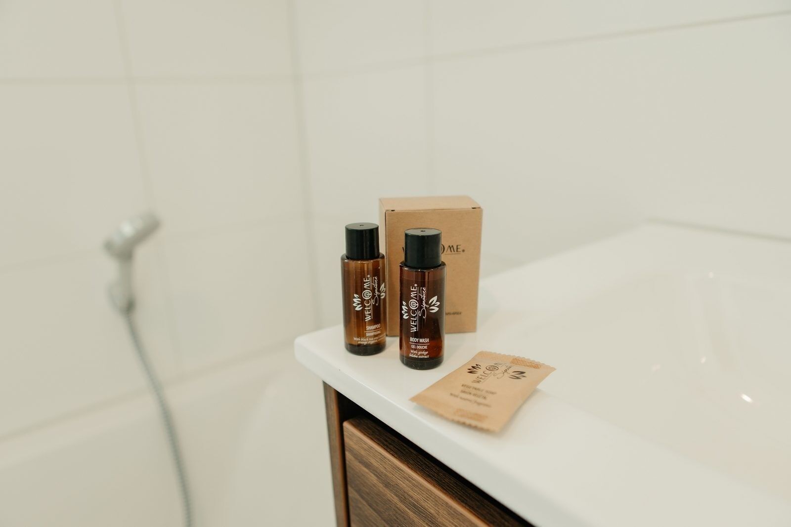 Une salle de bain avec un comptoir blanc, deux bouteilles de shampoing, une bouteille de gel douche et une boîte.