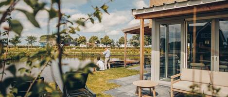 A modern house with a glass conservatory, a pond, and a patio with outdoor furniture.