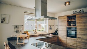 A modern kitchen with a large island, built-in oven, and a window overlooking a garden. - Parc Pharshoeke - Meervilla Deluxe met Sauna | 8p (Heeg)