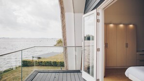 A balcony with a view of the sea, a glass door leading to a bedroom with a bed and wardrobe. - Parc Pharshoeke - Meervilla Deluxe met Sauna | 8p (Heeg)
