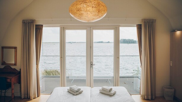 A bedroom with two beds, a large window with curtains, a wooden desk, and a hanging light fixture. - Parc Pharshoeke - Meervilla Deluxe met Sauna | 8p (Heeg)