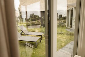 Un área de estar moderna al aire libre con una división de vidrio, un césped y vistas a un edificio.
