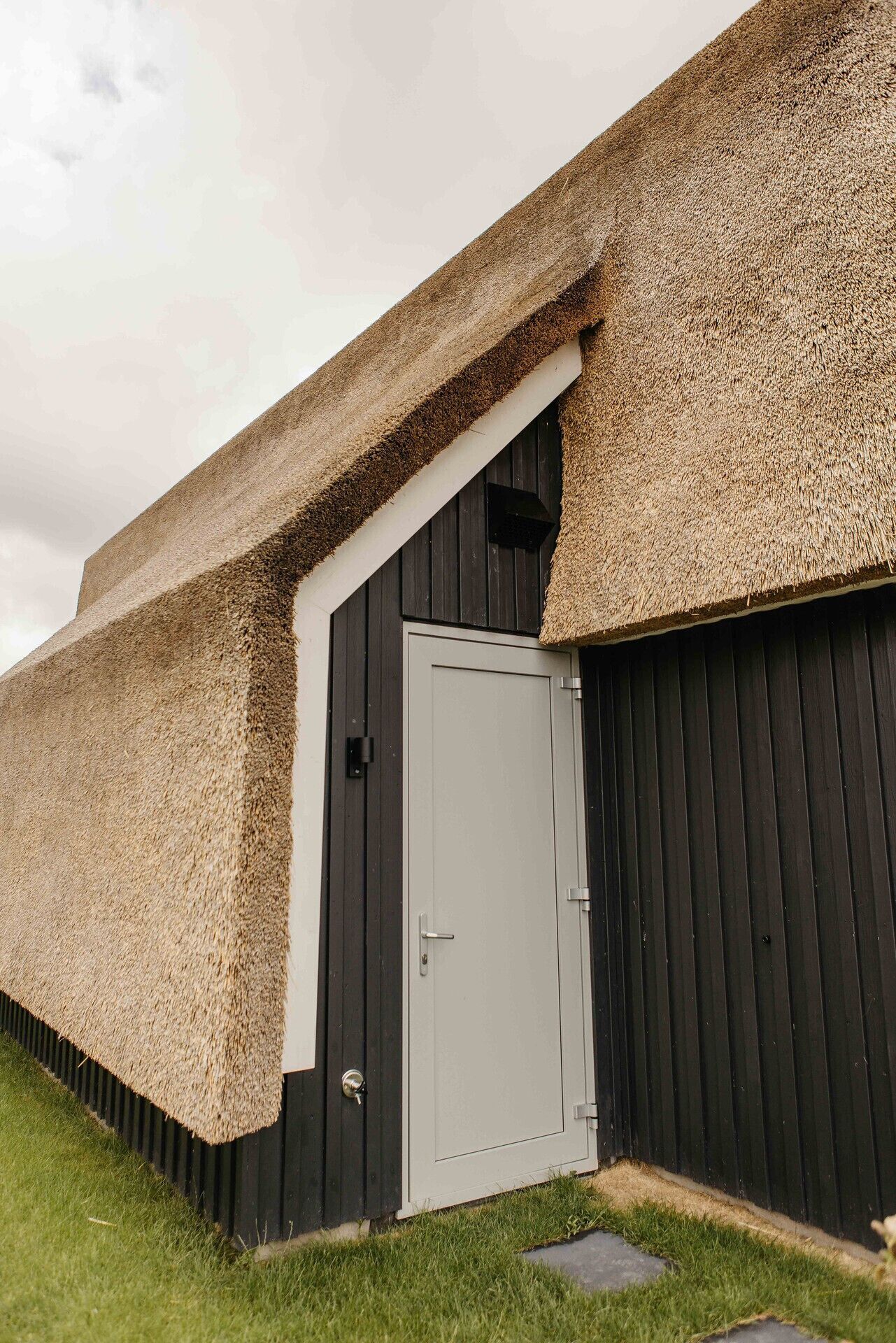 A building with a grey door, a black exterior wall, and a thatched roof.