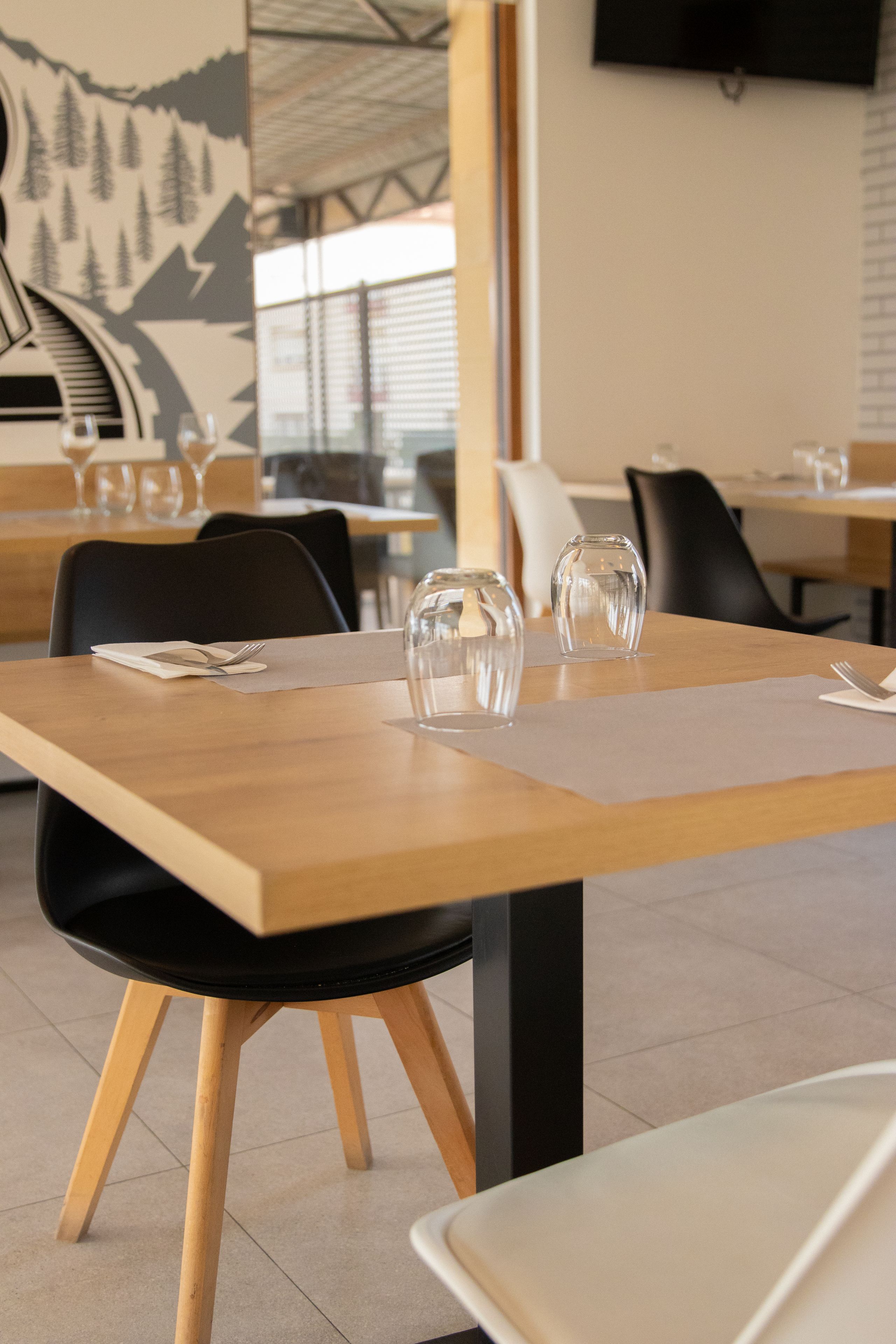 Ein Restaurantinneres mit Holztischen, schwarzen Stühlen und klarem Glas auf den Tischen.