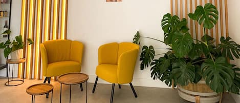 A room with two yellow armchairs, a wooden coffee table, and a large potted monstera plant.