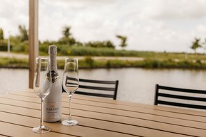 A bottle of Calvet wine and two glasses on a wooden table by a body of water. - Parc Pharshoeke - Watervilla buitenzijde | 8p (Heeg)