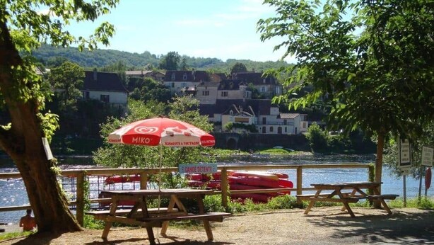 Picnicområde ved søen med bænke, en rød parasol og kanoer.