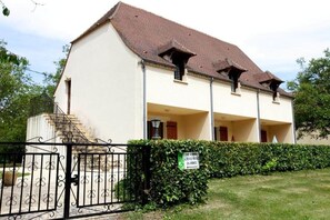 A two-story building with a tiled roof, a staircase leading to the entrance, and a sign indicating a public space. - Studio C* Ferme du Port d'Enveaux* on the banks of the Dordogne (Saint-Vincent-de-Cosse)