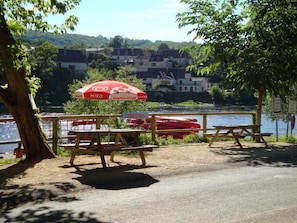 A lakeside picnic area with benches, a red umbrella, and canoes. - Studio C* Ferme du Port d'Enveaux* on the banks of the Dordogne (Saint-Vincent-de-Cosse)