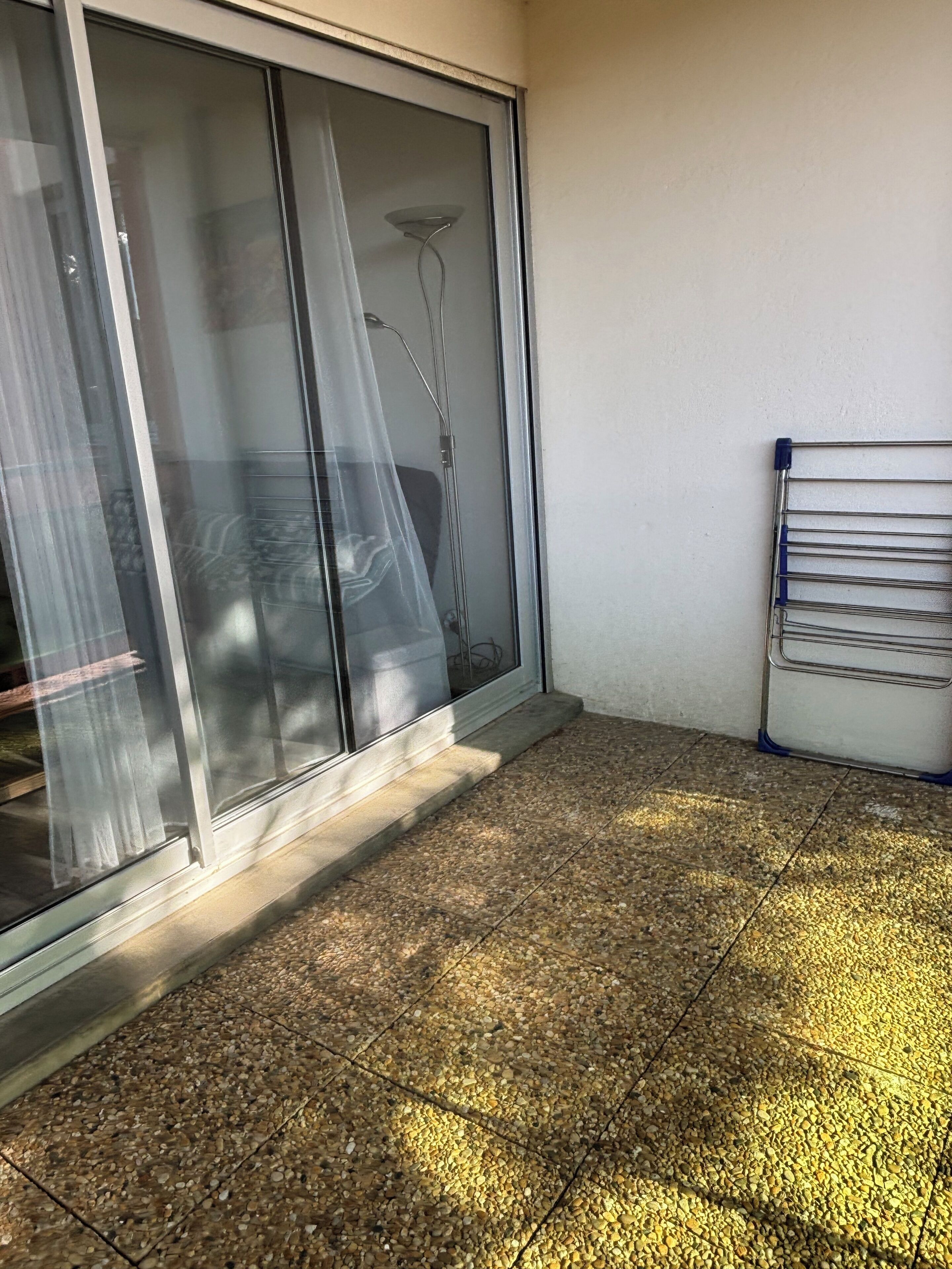 A room with a sliding glass door, a metal drying rack, and a tiled floor.