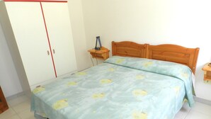 Une chambre à coucher comprenant un lit, une table de chevet en bois, une armoire et une petite table.
