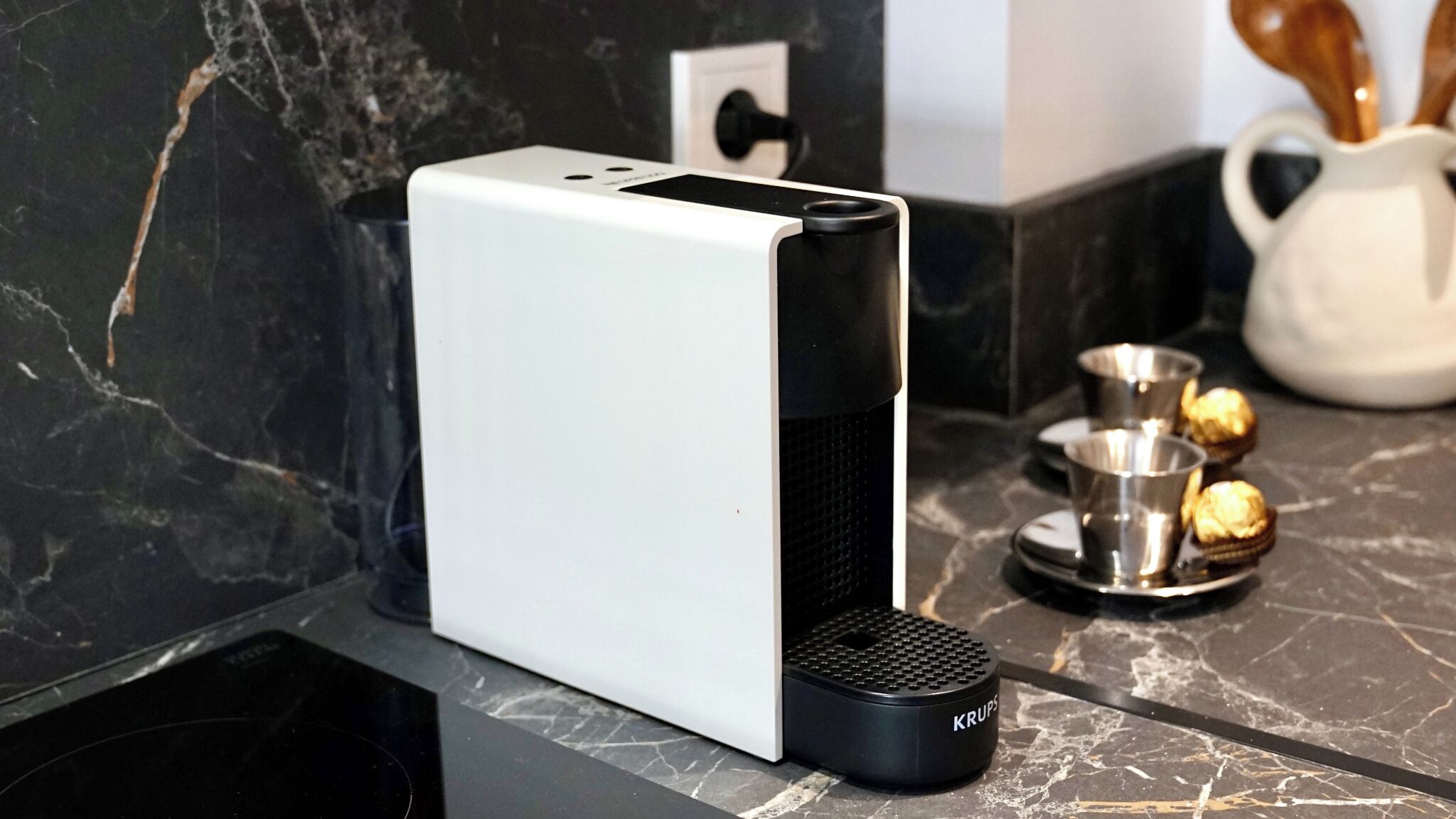 A modern kitchen with a white appliance, a black Krups coffee maker, and a marble countertop.