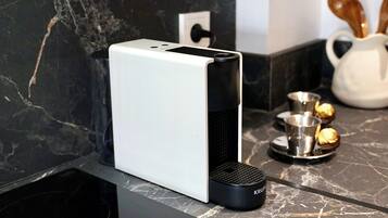 A modern kitchen with a white appliance, a black Krups coffee maker, and a marble countertop.