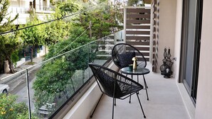 A balcony with two chairs and a small table, a railing, and a view of trees and buildings. - Alimos Escape 2 (Alimos)