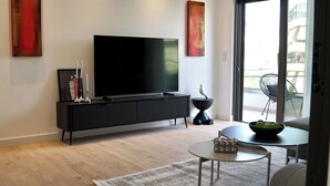A modern living room with a flat-screen TV, a black console, a round coffee table, and a balcony with outdoor furniture. - Alimos Escape 2 (Alimos)