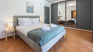 A bedroom with a bed, a nightstand, a wall-mounted lamp, a painting, and a sliding door leading to another room. - Casa Jasmine - Fenced Garden, Pool and Algarve Sun (Vale da Telha)