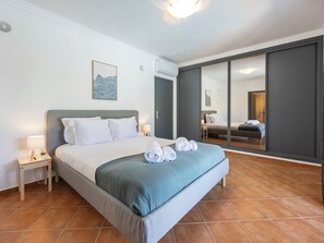A bedroom with a bed, a nightstand, a wall-mounted lamp, a painting, and a sliding door leading to another room. - Casa Jasmine - Fenced Garden, Pool and Algarve Sun (Vale da Telha)