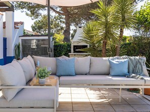 An outdoor seating area with a sofa, a table with a plant, and a grill. - Casa Jasmine - Fenced Garden, Pool and Algarve Sun (Vale da Telha)