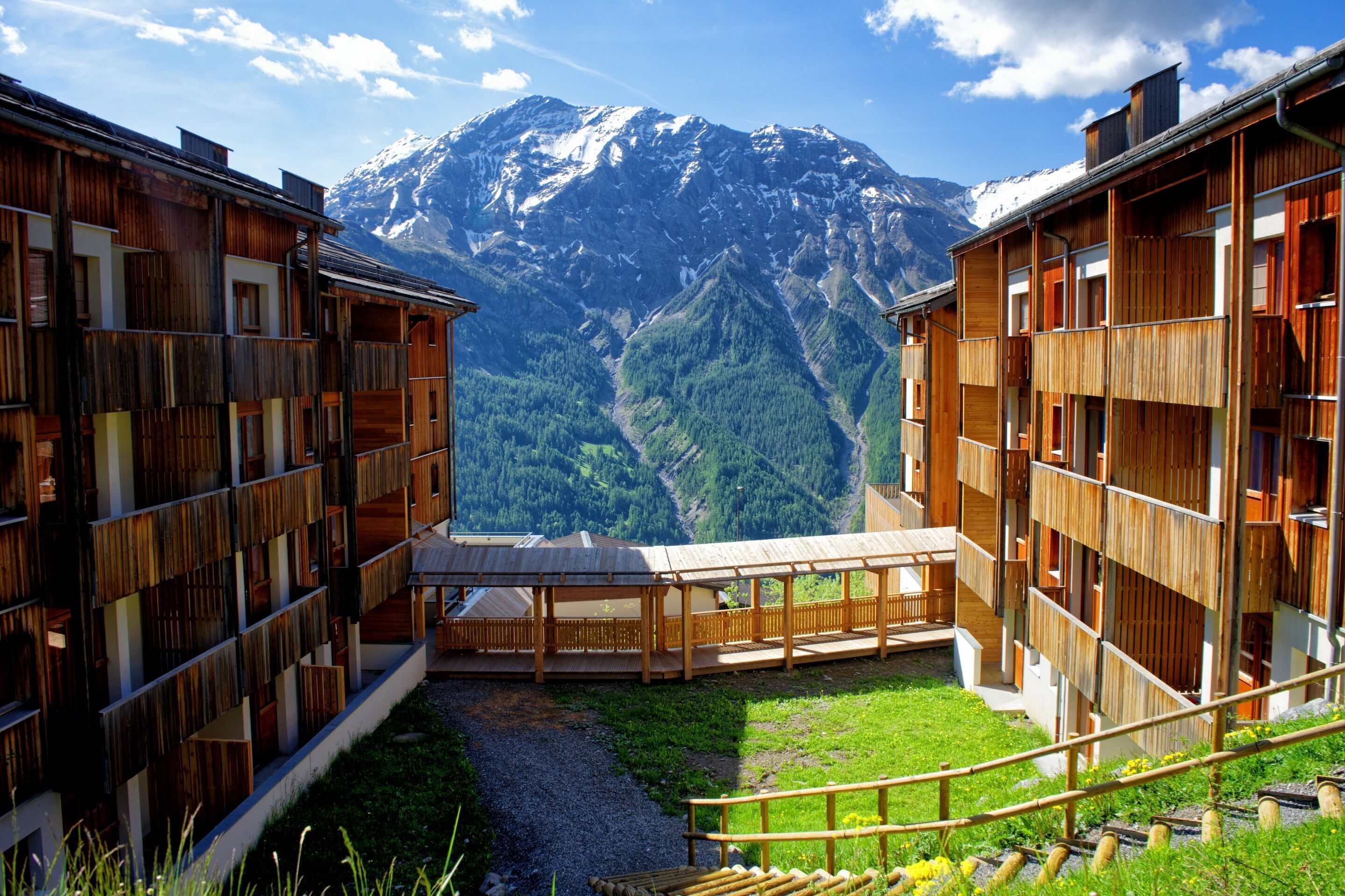 Un edificio in legno con numerosi balconi, un vialetto sterrato e vista sulle montagne.